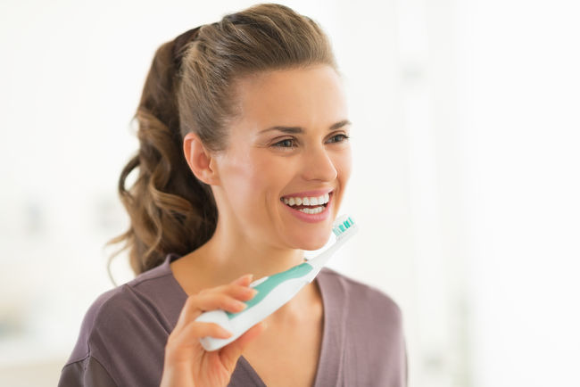 Žena si čistí zuby sonickým kartáčkem.